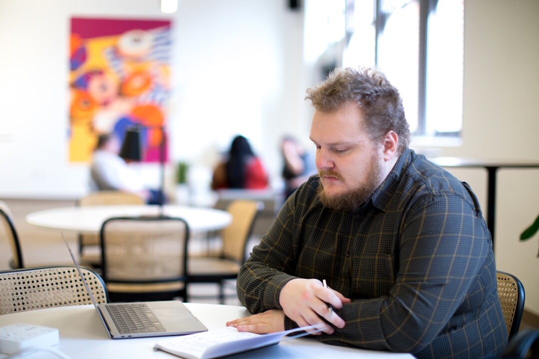 Person writing engaging content on laptop with notebook and coffee in bright workspace